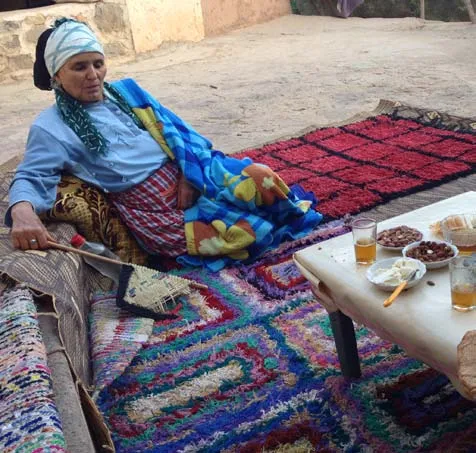 Woman seated beside vivid red and blue woven rugs