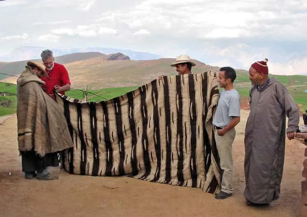 Four men holding a black-and-white striped textile in the landscape
