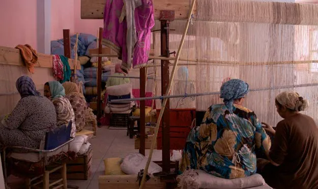 Women gathered around a vertical loom in a rural weaving workshop