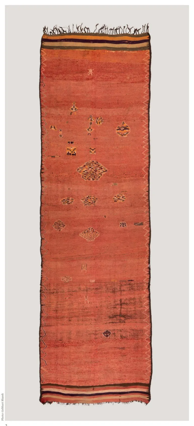 Long narrow rust-red rug with a sparse column of small geometric motifs