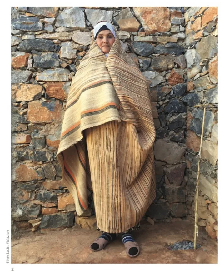 Ait Moussa woman wrapped in a pale striped haik against a stone wall