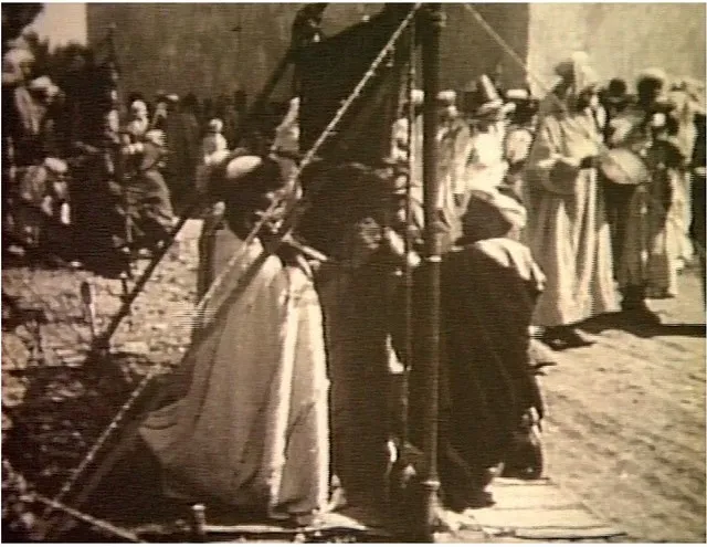Black-and-white film still of a master weaver and women at a loom